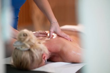 Spa 'da Sırt Masajı. Mavi üniformalı profesyonel bir masaj terapisti masaj masasında yatan bir müşteriye rahatlatıcı bir sırt masajı sağlar.