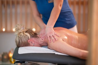 Spa 'da Sırt Masajı. Mavi üniformalı profesyonel bir masaj terapisti masaj masasında yatan bir müşteriye rahatlatıcı bir sırt masajı sağlar.