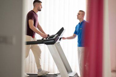 Adam içeride koşu bandında antrenör yardımıyla fizik tedavi görüyor..