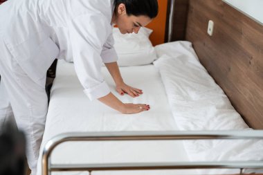 Üniformalı iki hemşire çarşafları değiştirerek ve hastalar için hijyenik bir ortam sağlayarak hastane odasını temizleyip düzenliyor.