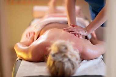 Spa 'da Sırt Masajı. Mavi üniformalı profesyonel bir masaj terapisti masaj masasında yatan bir müşteriye rahatlatıcı bir sırt masajı sağlar.