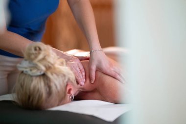 Spa 'da Sırt Masajı. Mavi üniformalı profesyonel bir masaj terapisti masaj masasında yatan bir müşteriye rahatlatıcı bir sırt masajı sağlar.