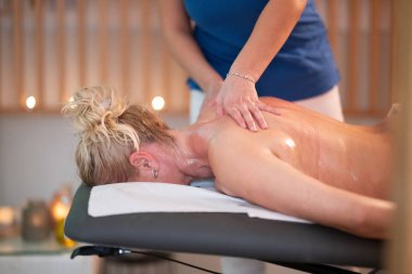 Spa 'da Sırt Masajı. Mavi üniformalı profesyonel bir masaj terapisti masaj masasında yatan bir müşteriye rahatlatıcı bir sırt masajı sağlar.