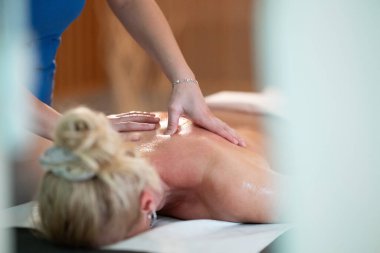 Spa 'da Sırt Masajı. Mavi üniformalı profesyonel bir masaj terapisti masaj masasında yatan bir müşteriye rahatlatıcı bir sırt masajı sağlar.