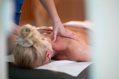 Spa 'da Sırt Masajı. Mavi üniformalı profesyonel bir masaj terapisti masaj masasında yatan bir müşteriye rahatlatıcı bir sırt masajı sağlar.