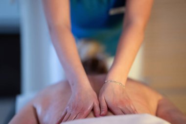 Spa 'da Sırt Masajı. Mavi üniformalı profesyonel bir masaj terapisti masaj masasında yatan bir müşteriye rahatlatıcı bir sırt masajı sağlar.