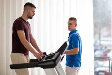 Adam içeride koşu bandında antrenör yardımıyla fizik tedavi görüyor..