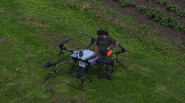 Yeşil bir alanda büyük bir tarımsal aracın bataryasını değiştiren bir kadın çiftçinin hava görüntüsü modern akıllı çiftçilik, insansız hava aracı teknolojisi ve hassas tarım yenilikleri sergiliyor. 