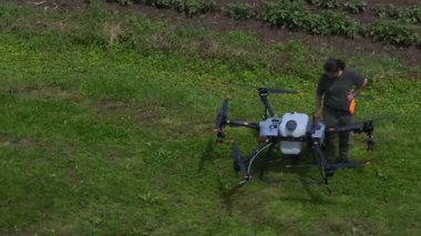 Yeşil bir alanda büyük bir tarımsal aracın bataryasını değiştiren bir kadın çiftçinin hava görüntüsü modern akıllı çiftçilik, insansız hava aracı teknolojisi ve hassas tarım yenilikleri sergiliyor. 