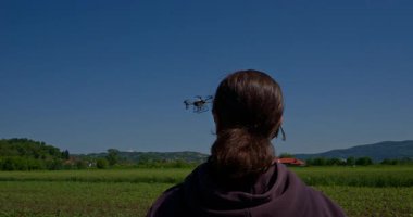 Yenilikçi bir dişi çiftçi, günbatımında bir tarlanın ortasında dikilirken, tarım arazilerini modern akıllı tarım uygulamalarının bir parçası olarak incelemek ve izlemek için hava teknolojisini kullanır..