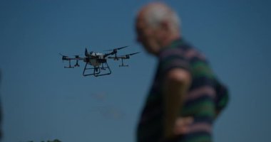 Yenilikçi bir çiftçi, günbatımında bir tarlanın ortasında dikilirken, tarım arazilerini modern akıllı tarım uygulamalarının bir parçası olarak incelemek ve tarlaları izlemek için hava teknolojisini kullanır..