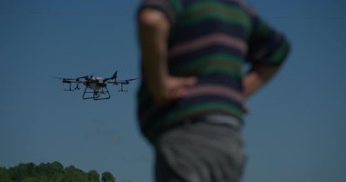 Yenilikçi bir çiftçi, günbatımında bir tarlanın ortasında dikilirken, tarım arazilerini modern akıllı tarım uygulamalarının bir parçası olarak incelemek ve tarlaları izlemek için hava teknolojisini kullanır..