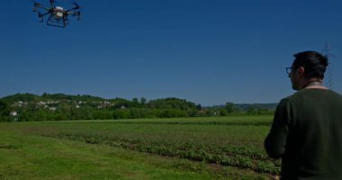 Yenilikçi bir çiftçi, günbatımında bir tarlanın ortasında dikilirken, tarım arazilerini modern akıllı tarım uygulamalarının bir parçası olarak incelemek ve tarlaları izlemek için hava teknolojisini kullanır..