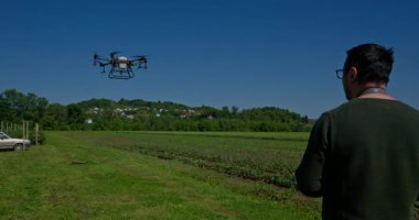 Yenilikçi bir çiftçi, günbatımında bir tarlanın ortasında dikilirken, tarım arazilerini modern akıllı tarım uygulamalarının bir parçası olarak incelemek ve tarlaları izlemek için hava teknolojisini kullanır..
