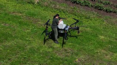 Yeşil bir alanda büyük bir tarımsal aracın bataryasını değiştiren bir kadın çiftçinin hava görüntüsü modern akıllı çiftçilik, insansız hava aracı teknolojisi ve hassas tarım yenilikleri sergiliyor. 