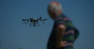 Yenilikçi bir çiftçi, günbatımında bir tarlanın ortasında dikilirken, tarım arazilerini modern akıllı tarım uygulamalarının bir parçası olarak incelemek ve tarlaları izlemek için hava teknolojisini kullanır..