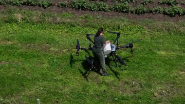 Yeşil bir alanda büyük bir tarımsal aracın bataryasını değiştiren bir kadın çiftçinin hava görüntüsü modern akıllı çiftçilik, insansız hava aracı teknolojisi ve hassas tarım yenilikleri sergiliyor. 