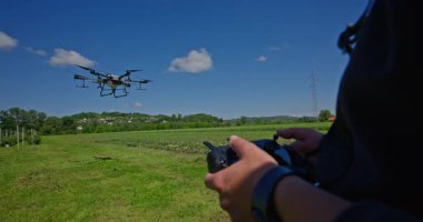 Yenilikçi bir çiftçi, günbatımında bir tarlanın ortasında dikilirken, tarım arazilerini modern akıllı tarım uygulamalarının bir parçası olarak incelemek ve tarlaları izlemek için hava teknolojisini kullanır..