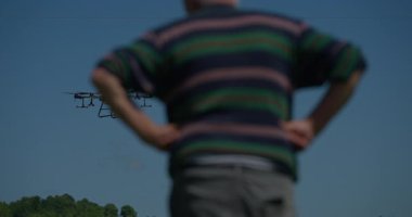 Yenilikçi bir çiftçi, günbatımında bir tarlanın ortasında dikilirken, tarım arazilerini modern akıllı tarım uygulamalarının bir parçası olarak incelemek ve tarlaları izlemek için hava teknolojisini kullanır..