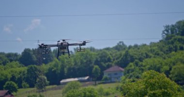 Kırsal ortamlardaki gelişmiş tarım teknolojisi ve hassas tarım tekniklerini vurgulayarak, ekin izleme veya spreyleme görevi sırasında ekili bir tarla üzerinde uçan hava aracı..