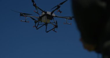 Yenilikçi bir çiftçi, günbatımında bir tarlanın ortasında dikilirken, tarım arazilerini modern akıllı tarım uygulamalarının bir parçası olarak incelemek ve tarlaları izlemek için hava teknolojisini kullanır..