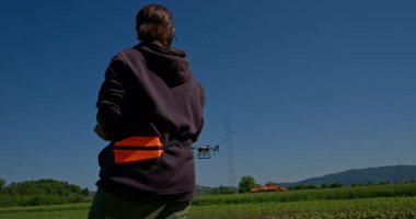 Yenilikçi bir dişi çiftçi, günbatımında bir tarlanın ortasında dikilirken, tarım arazilerini modern akıllı tarım uygulamalarının bir parçası olarak incelemek ve izlemek için hava teknolojisini kullanır..