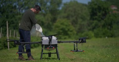 Modern yenilikçi çiftçi büyük bir tarım aracını yeşil alanda sıvı gübrelerle dolduruyor, modern akıllı çiftçilik, dron teknolojisi ve hassas tarım sergiliyor.