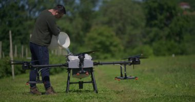 Modern yenilikçi çiftçi büyük bir tarım aracını yeşil alanda sıvı gübrelerle dolduruyor, modern akıllı çiftçilik, dron teknolojisi ve hassas tarım sergiliyor.