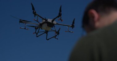 Yenilikçi bir çiftçi, günbatımında bir tarlanın ortasında dikilirken, tarım arazilerini modern akıllı tarım uygulamalarının bir parçası olarak incelemek ve tarlaları izlemek için hava teknolojisini kullanır..