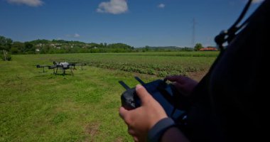 Yenilikçi bir çiftçi, günbatımında bir tarlanın ortasında dikilirken, tarım arazilerini modern akıllı tarım uygulamalarının bir parçası olarak incelemek ve tarlaları izlemek için hava teknolojisini kullanır..
