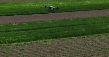 Kırsal ortamlardaki gelişmiş tarım teknolojisi ve hassas tarım tekniklerini vurgulayarak, ekin izleme veya spreyleme görevi sırasında ekili bir tarla üzerinde uçan hava aracı..