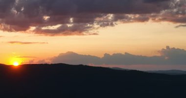 Gün batımında parlayan güneş, sıcak turuncu gökyüzü ve uzun çam ağaçları olan manzaralı orman silueti. Huzurlu, sakin doğa manzarası sakinlik, sükunet ve güzellik temaları için mükemmeldir.