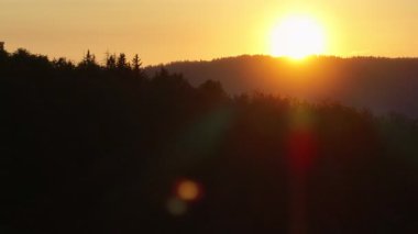 Scenic forest silhouette at sunset with glowing sun on the horizon, warm orange sky, and tall pine trees. A peaceful, tranquil nature landscape perfect for themes of calm, serenity, and beauty