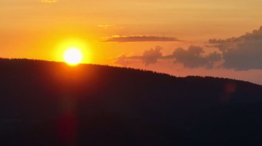 Gün batımında parlayan güneş, sıcak turuncu gökyüzü ve uzun çam ağaçları olan manzaralı orman silueti. Huzurlu, sakin doğa manzarası sakinlik, sükunet ve güzellik temaları için mükemmeldir.