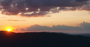 Gün batımında parlayan güneş, sıcak turuncu gökyüzü ve uzun çam ağaçları olan manzaralı orman silueti. Huzurlu, sakin doğa manzarası sakinlik, sükunet ve güzellik temaları için mükemmeldir.
