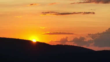 Gün batımında parlayan güneş, sıcak turuncu gökyüzü ve uzun çam ağaçları olan manzaralı orman silueti. Huzurlu, sakin doğa manzarası sakinlik, sükunet ve güzellik temaları için mükemmeldir.