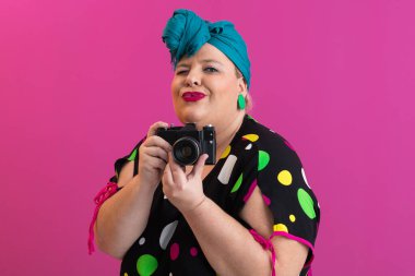 Ekranda pembe arka planda poz veren, kameralı, iri yarı, komik bir kadın.. 