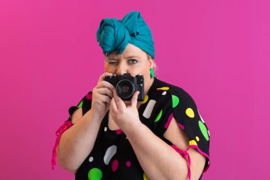 Ekranda pembe arka planda poz veren, kameralı, iri yarı, komik bir kadın.. 