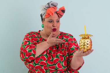 Karpuz desenli elbisesi olan, elleri açık, açık ve açık mavi arkaplan önünde şaşkın, şaşkın bir yüz ifadesi sergileyen neşeli, iri yarı bir kadın.. 