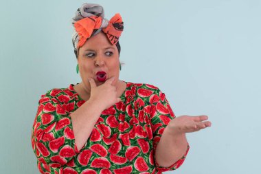 Karpuz desenli elbisesiyle açık avucuna komik ve şaşkın bakışlı açık mavi arkaplana bakan etkileyici ve iri yarı kadın.. 