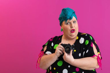 Elinde kamera olan ve sürpriz yapan etkileyici, iri yarı bir kadın. Parlak renkli bir stüdyoda izole edilmiş.. 