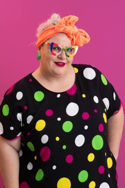 Artı canlı puantiyeli kadın. Pembe arka planda poz veriyor. Gözlük takıyor.. 