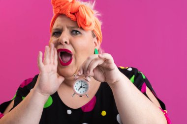 Pembe stüdyo arka planına karşı heyecan dolu parlak aksesuarlar ve canlı polka giysili neşeli, iri yarı kadın.. 