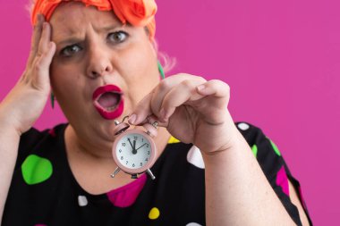 Pembe stüdyo arka planına karşı heyecan dolu parlak aksesuarlar ve canlı polka giysili neşeli, iri yarı kadın.. 