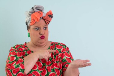 Karpuz desenli elbisesiyle açık avucuna komik ve şaşkın bakışlı açık mavi arkaplana bakan etkileyici ve iri yarı kadın.. 