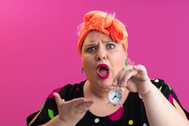 Pembe stüdyo arka planına karşı heyecan dolu parlak aksesuarlar ve canlı polka giysili neşeli, iri yarı kadın.. 