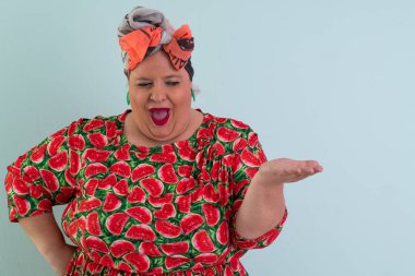 Karpuz desenli elbisesiyle açık avucuna komik ve şaşkın bakışlı açık mavi arkaplana bakan etkileyici ve iri yarı kadın.. 