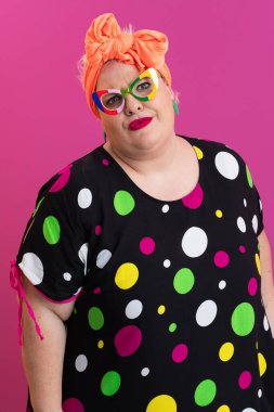 Artı canlı puantiyeli kadın. Pembe arka planda poz veriyor. Gözlük takıyor.. 