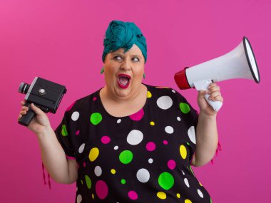 Canlı pembe bir arkaplan önünde elinde eski model bir kamerayla megafona bağıran komik, iri yarı bir kadın.. 