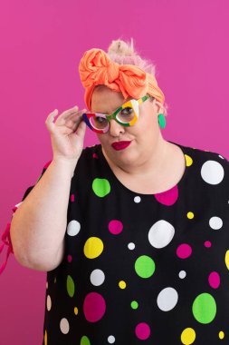 Artı canlı polka noktalı elbise giyen, güneş gözlüğü takan, pembe arka planda duran, boyunda bir kadın.. 